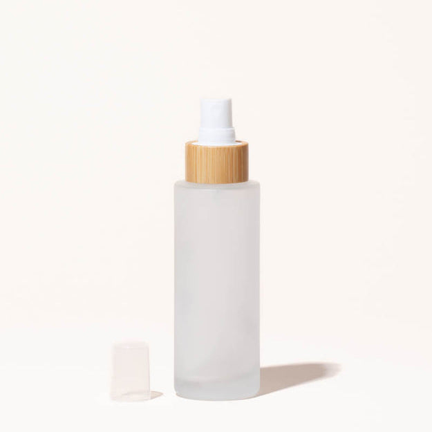 Simply Zero Forever Spray Bottle in frosted glass with bamboo collar and fine-mist pump, 3.4 oz, shown with pump cap removed on a cream background