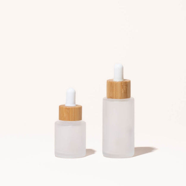 Simply Zero Forever Dropper Bottle in frosted glass with bamboo cap, shown in both sizes — .7 oz and 1.3 oz — on a cream background